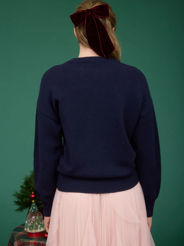 Person wearing a navy sweater and pink skirt with a green background