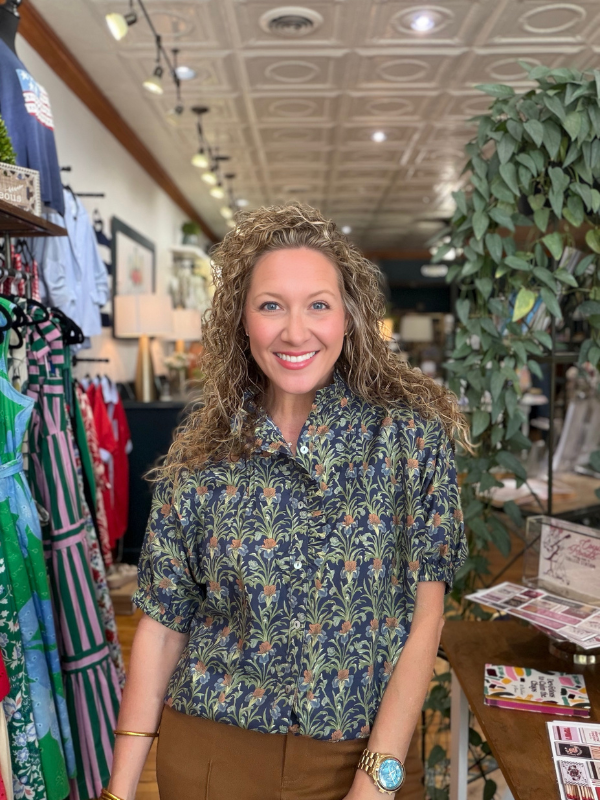 Woman standing in a clothing store wearing a patterned shirt.