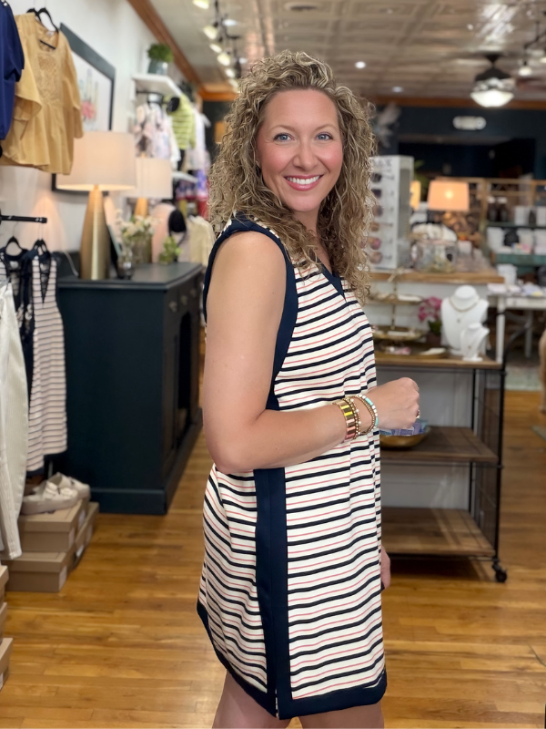 Woman in a striped dress standing in a store with wooden floors and shelves.
