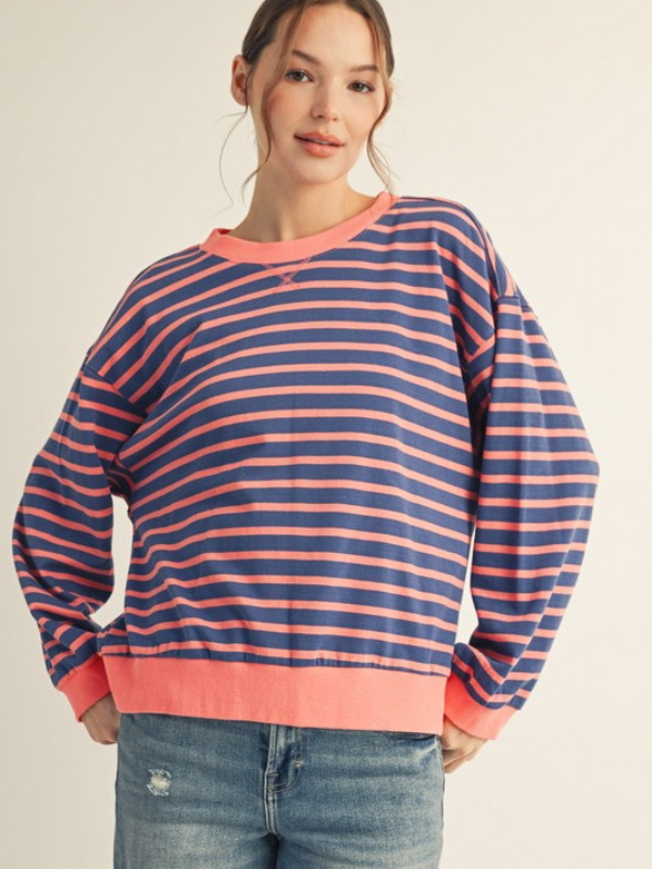 Woman wearing a blue and pink striped sweater with jeans on a beige background