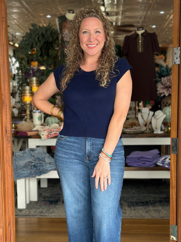 Woman wearing a navy blue top and blue jeans standing in a store.