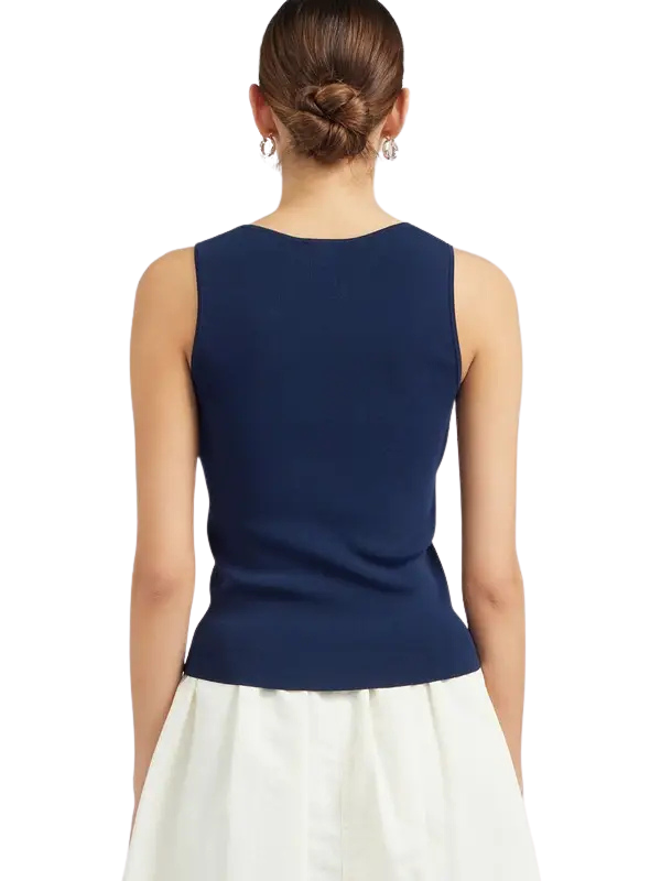 A woman shown from the back wearing a sleeveless navy blue top and a white skirt against a plain white background.