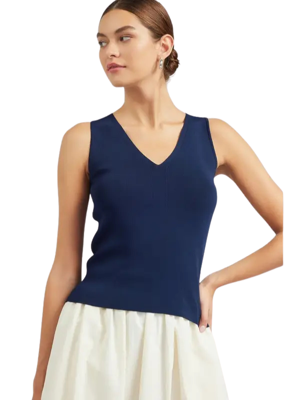 A woman wearing a sleeveless navy blue V-neck knit top and a cream-colored skirt, shown from the waist up against a plain white background.