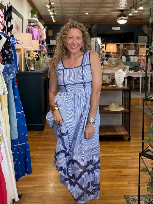 Woman in a blue dress standing in a store with clothing racks and products in the background.