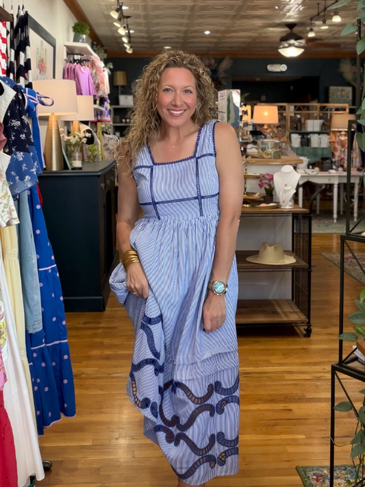 Woman in a blue dress standing in a store with clothing racks and products in the background.