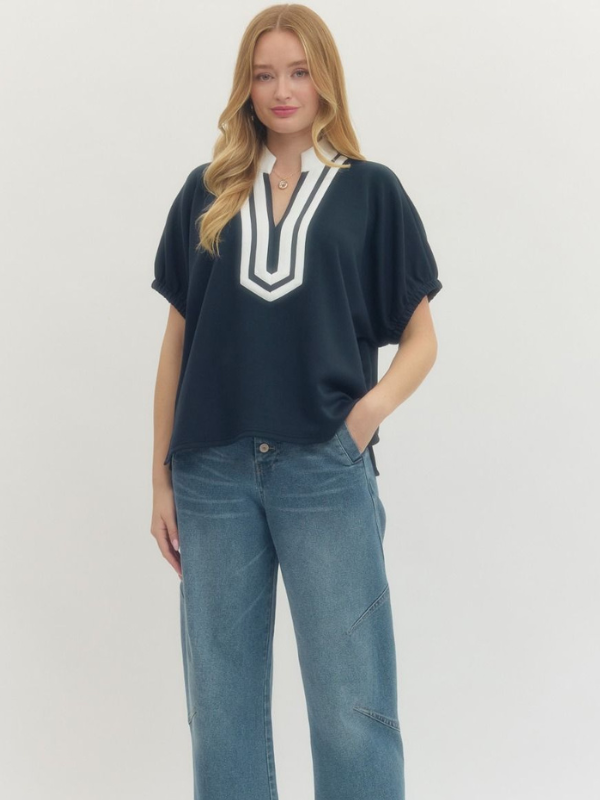 Woman wearing a navy top with a white V-neckline and blue jeans on a light gray background