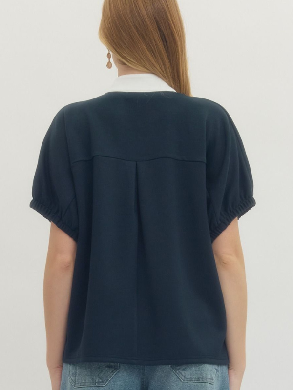 Person wearing a navy blue top with short sleeves on a plain background