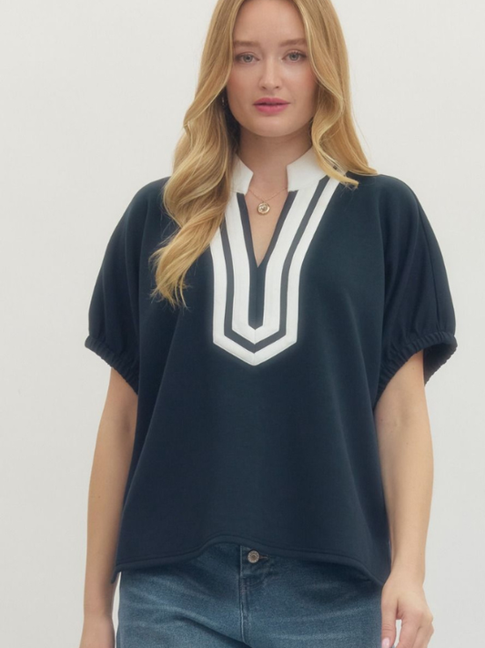 Woman wearing a navy blue top with a white V-neckline on a plain background