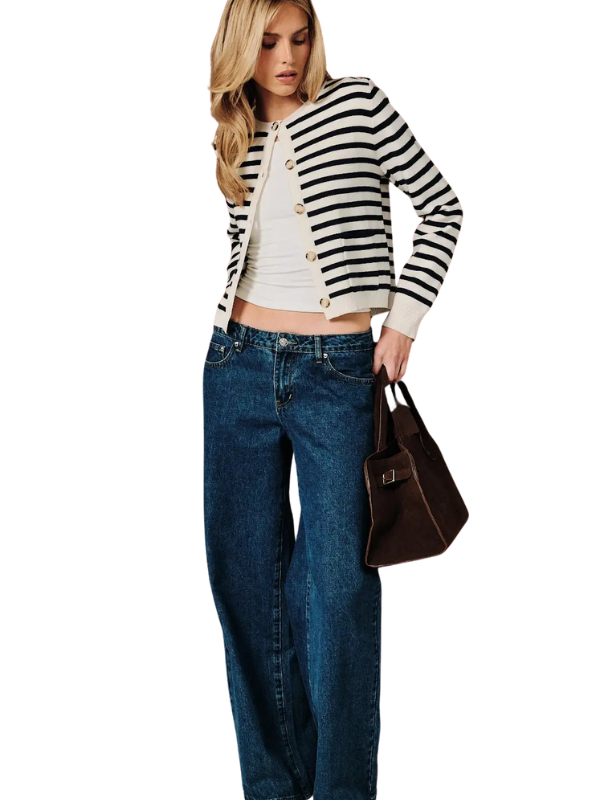 A woman modeling a black and white striped cardigan over a white crop top, paired with blue jeans and holding a brown leather handbag against a plain white background.