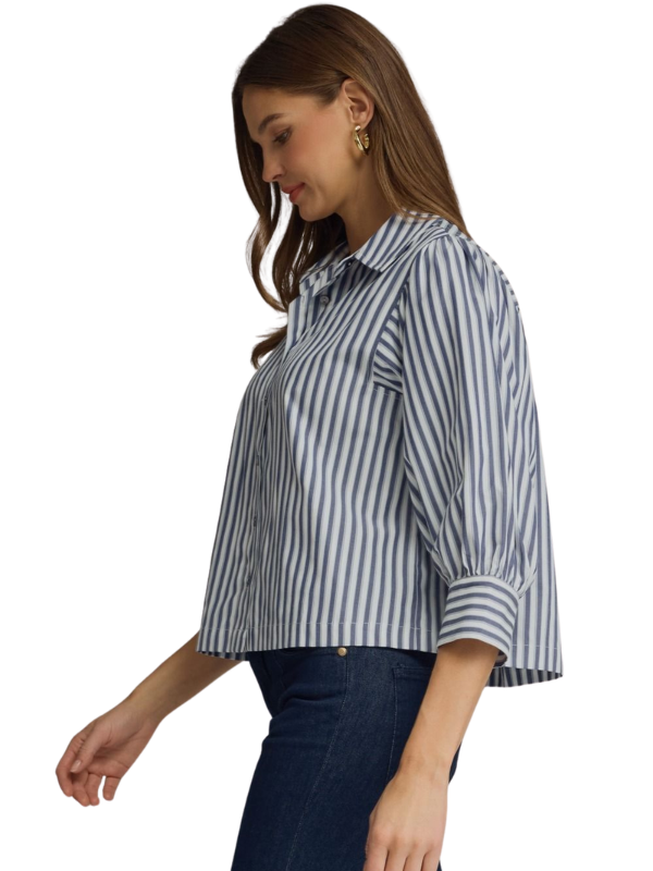 A woman wearing a blue and white vertically striped button-up shirt with three-quarter sleeves, paired with dark blue jeans, shown from a side profile against a plain white background.