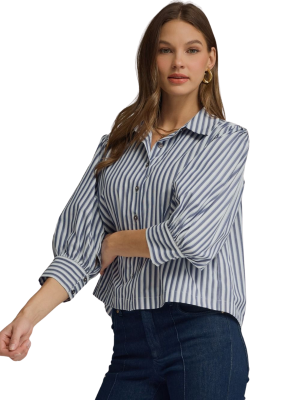 A woman wearing a blue and white vertically striped button-down blouse with three-quarter sleeves, paired with dark blue jeans, against a plain white background.