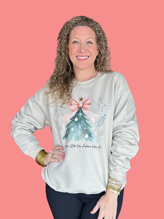 Woman wearing a light gray sweatshirt with a Christmas tree design on a pink background