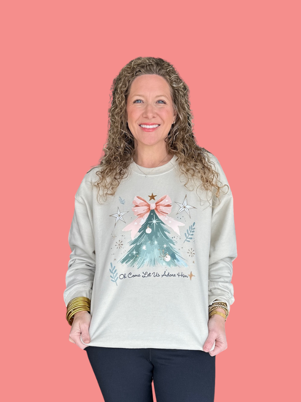 Woman wearing a light gray sweatshirt with a Christmas tree design on a pink background