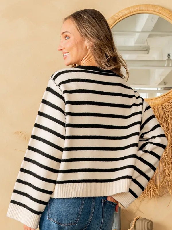 Woman wearing a black and white striped sweater in a room with a mirror and beige wall.