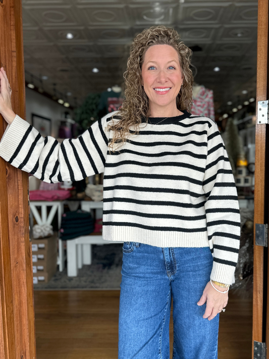 Woman wearing a black and white striped sweater and blue jeans standing inside a store.