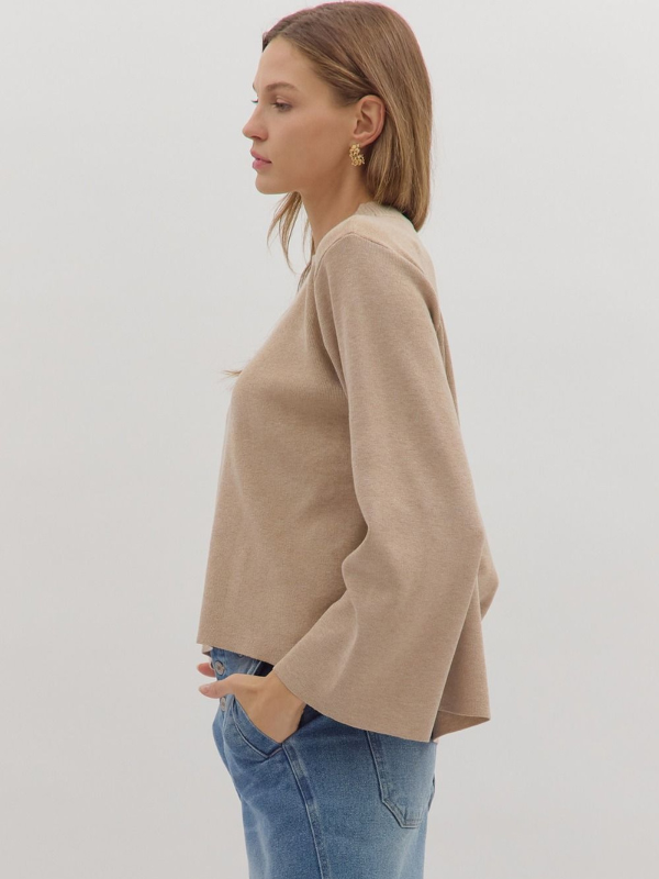 Woman wearing a beige sweater and blue jeans against a white background