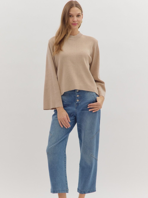 Woman wearing a beige sweater and blue jeans against a white background