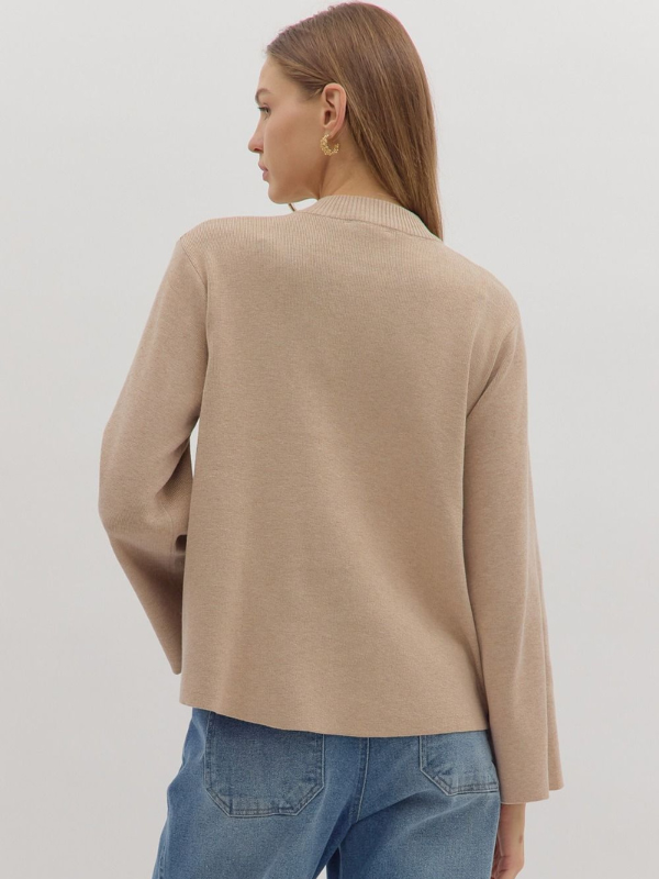 Woman wearing a beige sweater and blue jeans against a white background