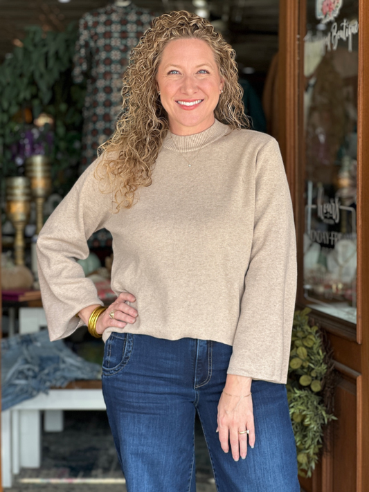 Woman wearing a beige sweater and blue jeans standing in a store.