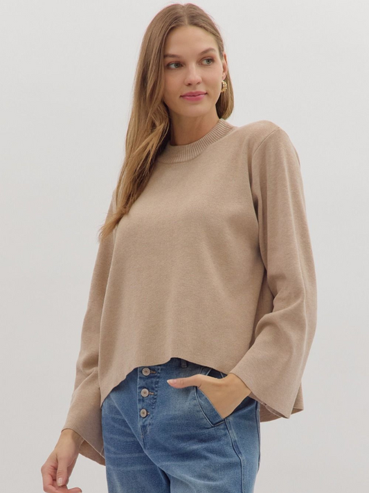 Woman wearing a beige sweater and blue jeans against a white background