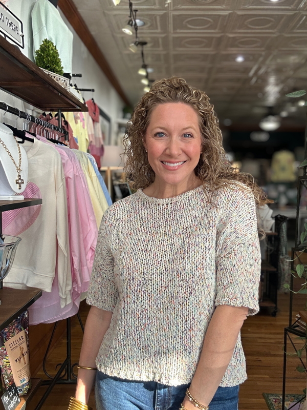 Woman standing in a clothing store wearing a patterned sweater.