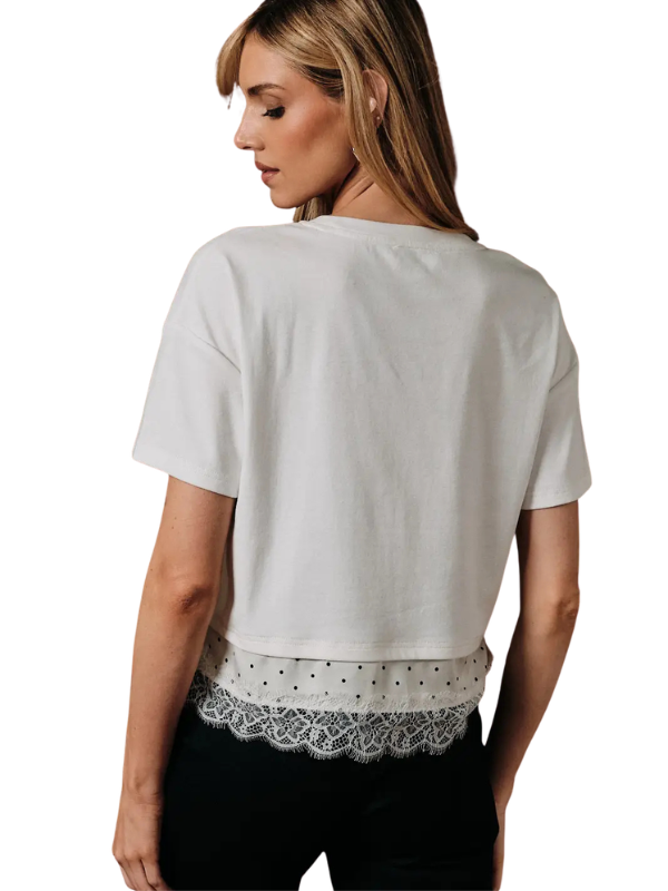 A woman shown from the back wearing a short-sleeve white crop top with a lace hem detail, paired with black pants, against a plain white background.