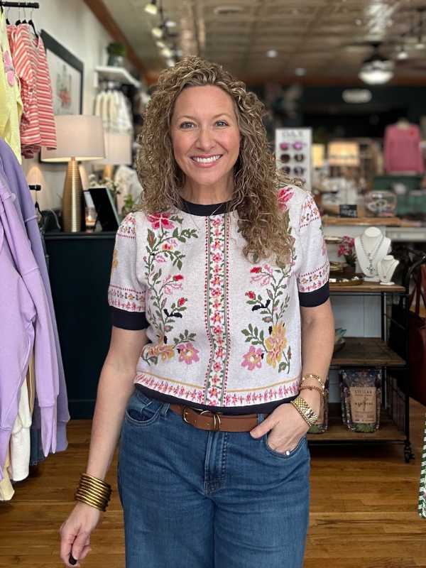 Woman wearing a floral embroidered top and blue jeans in a store setting