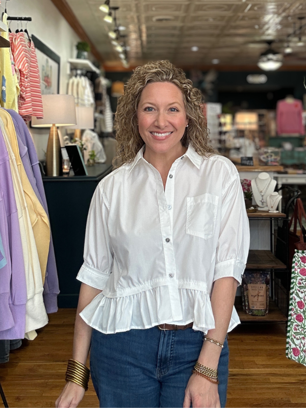 Woman wearing a white blouse with a peplum waist in a clothing store.