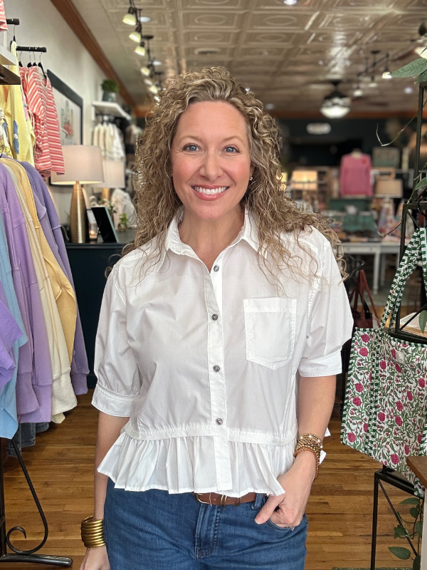 Woman wearing a white blouse with ruffled details in a clothing store.
