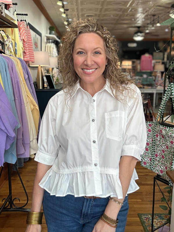 Woman wearing a white blouse with ruffled details in a clothing store.