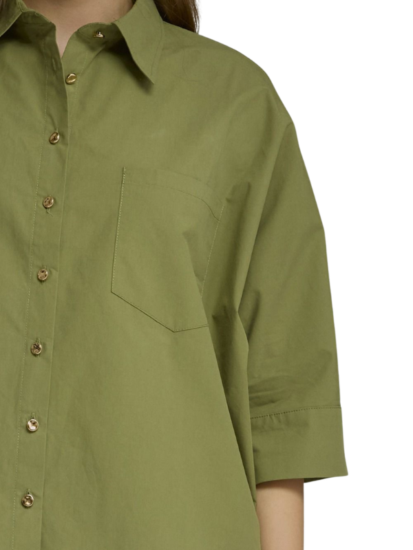Close-up of a person wearing an oversized olive green button-up shirt with a chest pocket and rolled sleeves, shown against a plain white background.