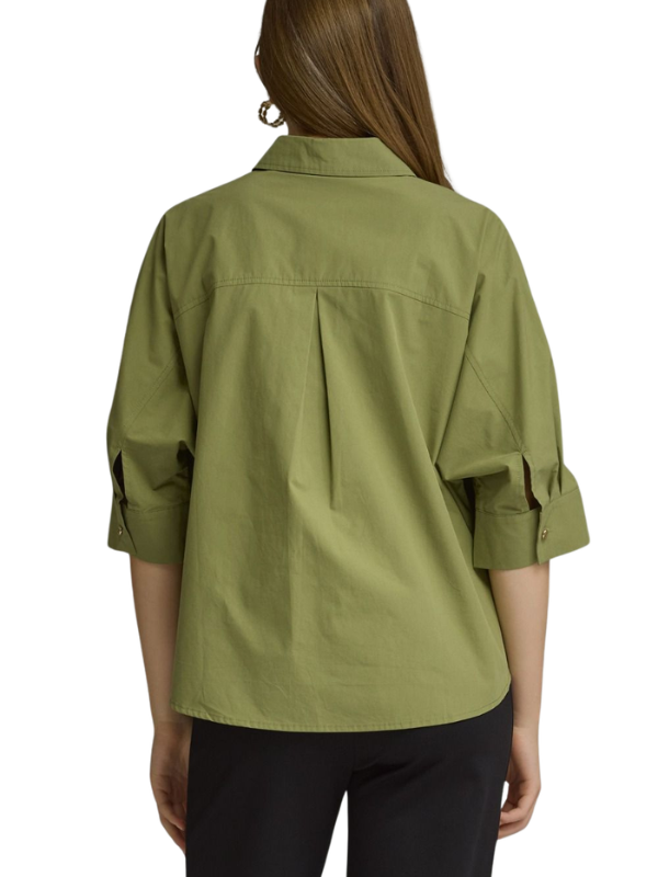 A woman shown from the back wearing an olive green button-up shirt with rolled three-quarter sleeves and black pants, against a plain white background.