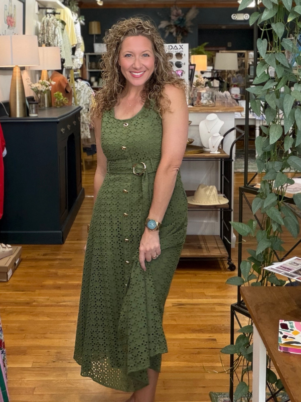Woman in a green dress standing in a store with plants and furniture.