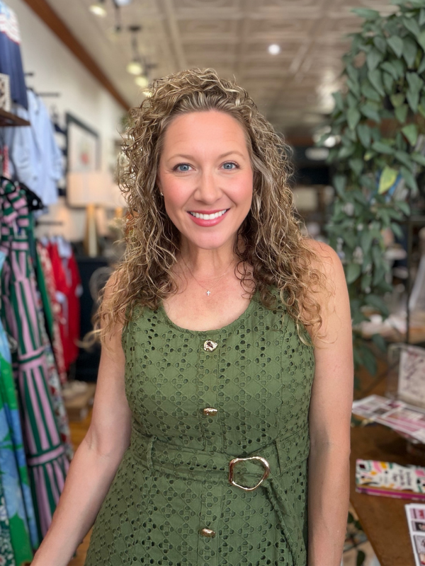 Woman in a green dress standing in a store with clothing and plants in the background