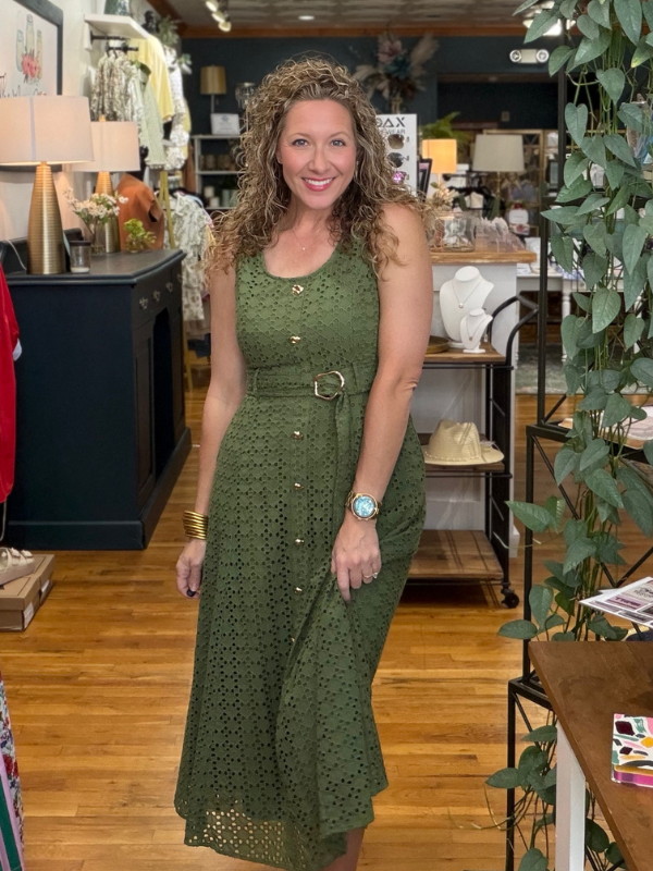 Woman in a green dress standing in a store with various items and decor around her.