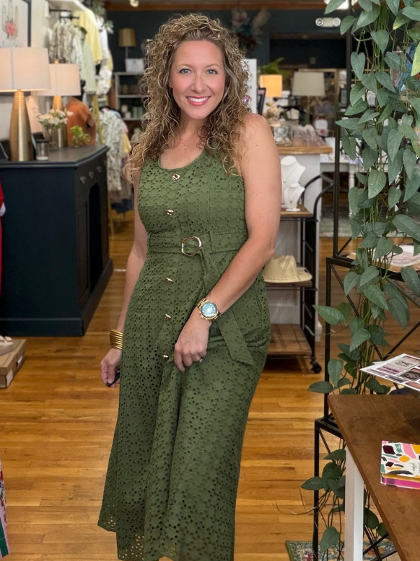 Woman in a green dress standing in a store with wooden floors and shelves.