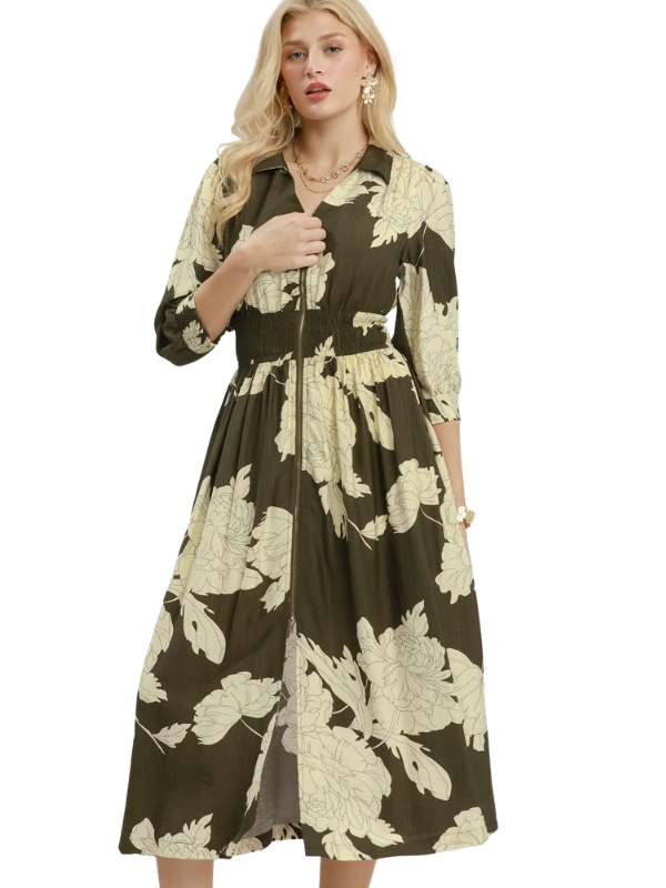 A woman modeling a mid-length button-front dress with three-quarter sleeves and a gathered waist, featuring a dark olive green and cream floral pattern against a plain white background.