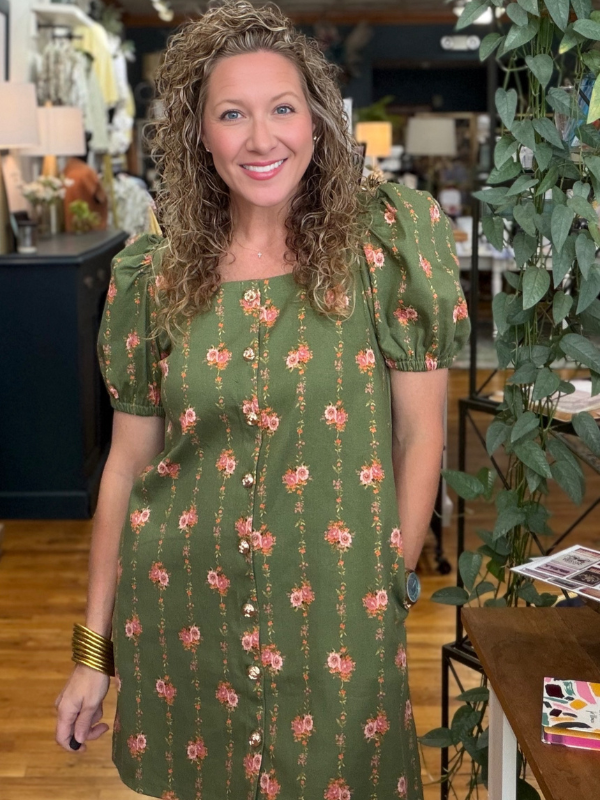 Woman wearing a green floral dress in an indoor setting with plants and furniture.