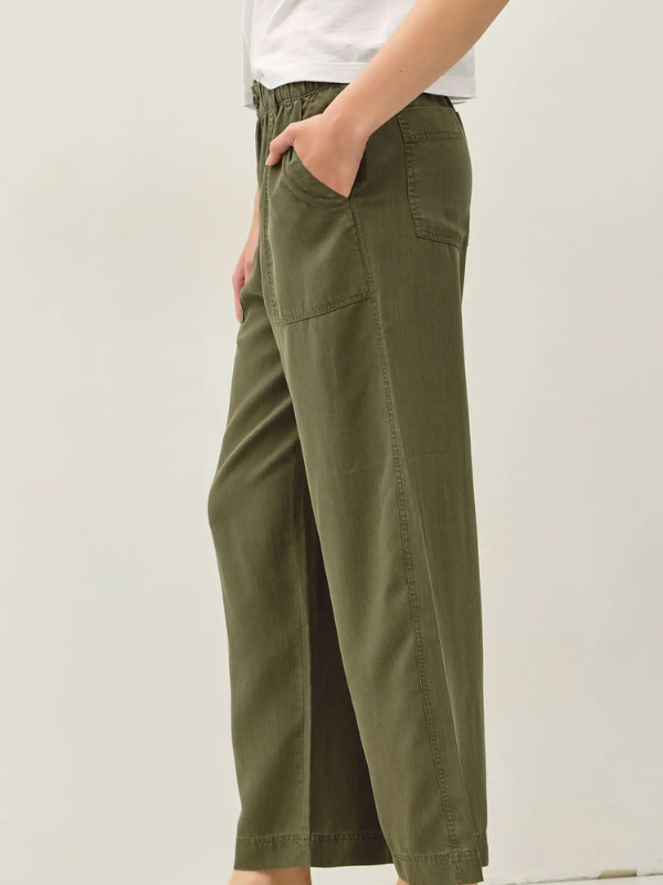A person wearing olive green wide-leg cropped pants with side pockets, paired with a white top, shown against a plain light background.