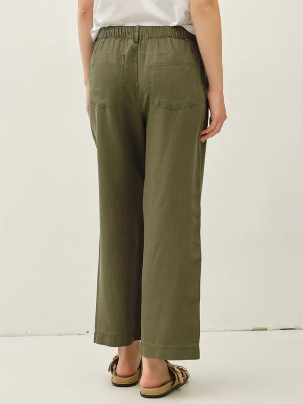 A person shown from the back wearing olive green wide-leg cropped pants, a white top, and brown slide sandals against a plain white studio background.