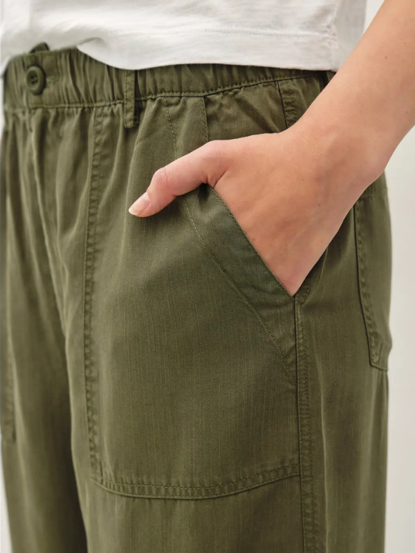 Close-up of a person wearing olive green wide-leg cargo pants with an elastic waistband, side button, and a hand tucked into a front pocket.