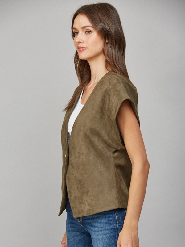 Woman wearing a green vest over a white top and blue jeans on a gray background