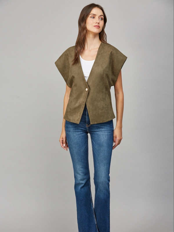 Woman wearing a green vest over a white top and blue jeans on a gray background