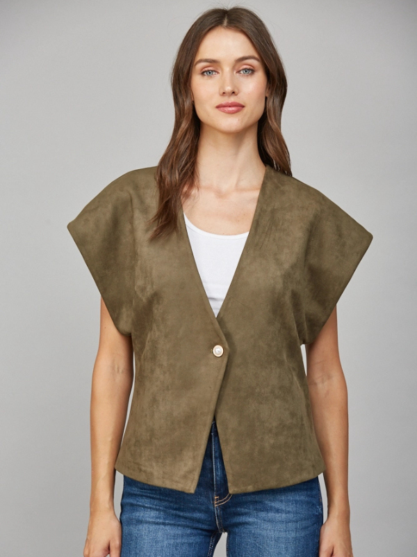 Woman wearing a brown suede vest over a white top and blue jeans on a gray background