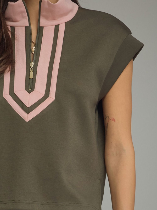Close-up of a person wearing a sleeveless olive green top with a pink mock neck, gold zipper, and pink chevron panel on the chest.