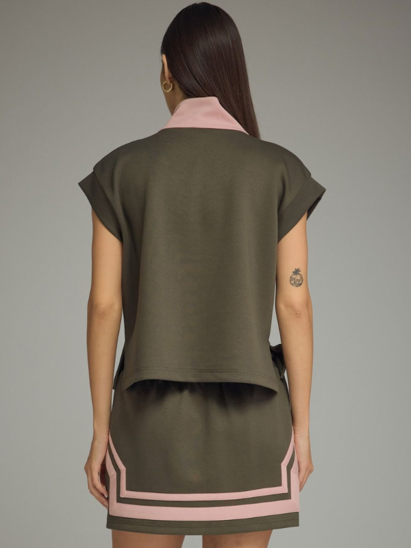 A model shown from the back wearing a dark olive green two-piece set consisting of a short-sleeve crop top and a matching mini skirt with light pink geometric border accents.