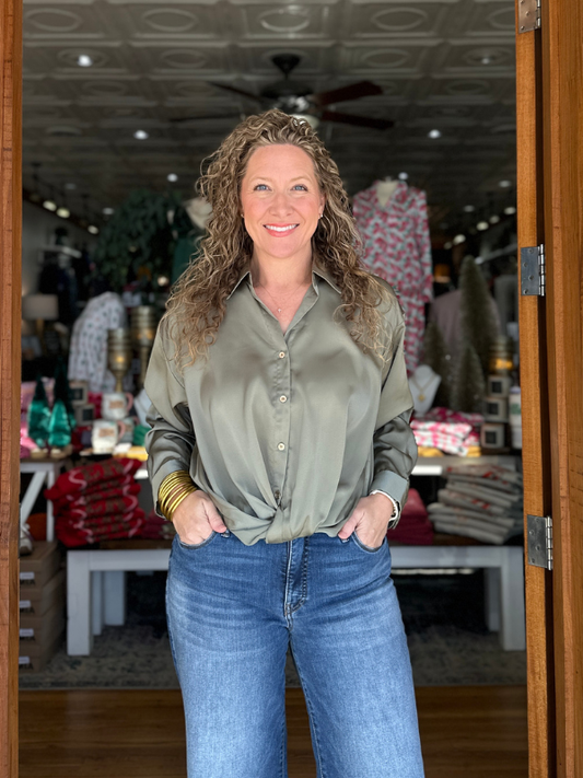 Woman standing in a store doorway wearing an olive green shirt and blue jeans.