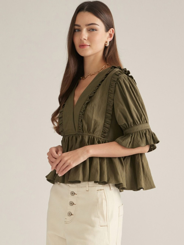woman wearing an olive v neck ruffle top and ecru pants