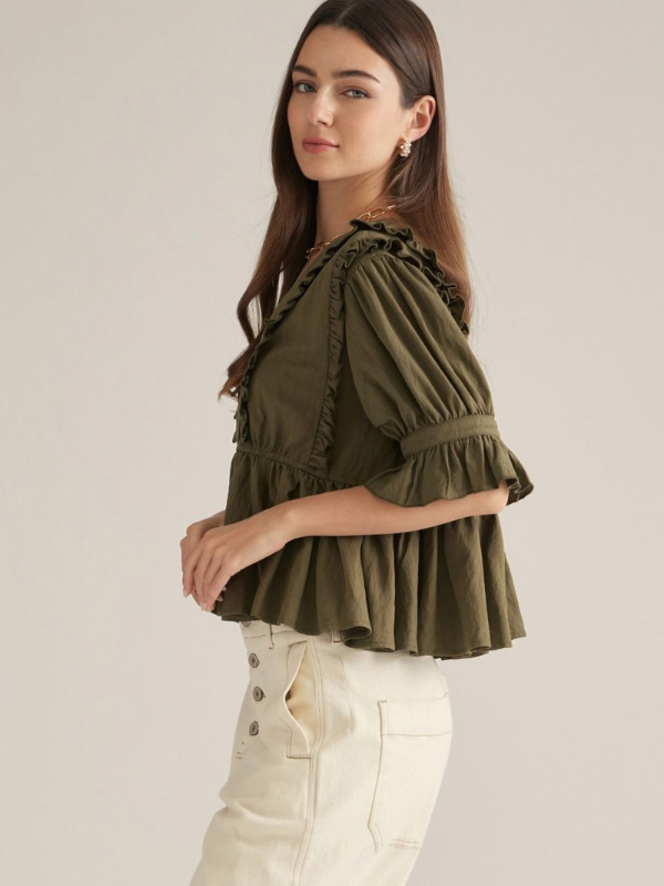 woman wearing an olive v neck ruffle top and ecru pants