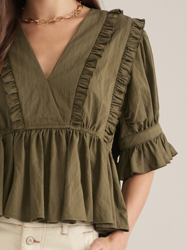 woman wearing an olive v neck ruffle top and ecru pants